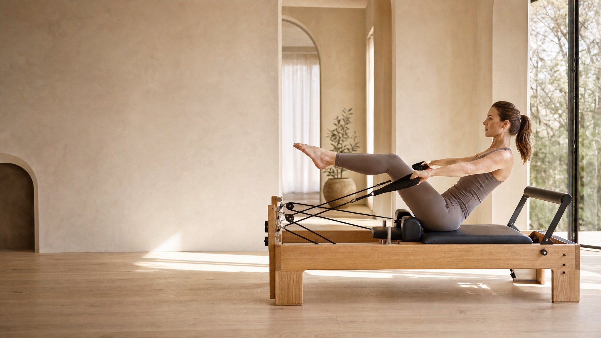 A woman using a wooden Pilates reformer in a warm private studio