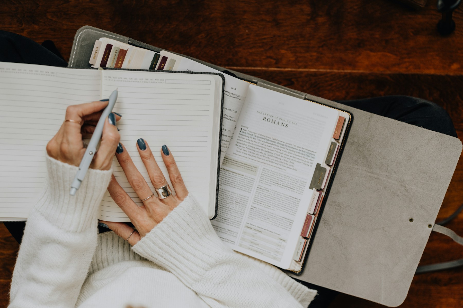 A woman writing in a journal beside an open Bible with page tabs