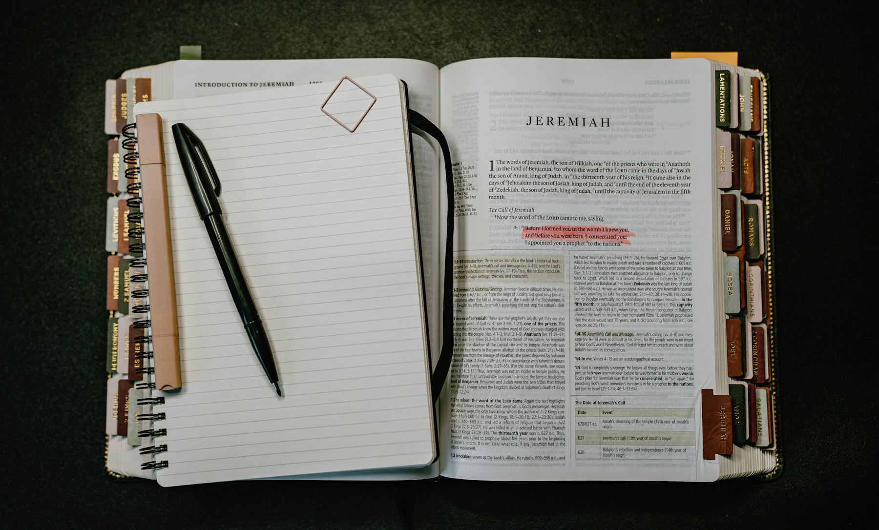 An open Bible with highlighted verse beside a lined notebook and pen