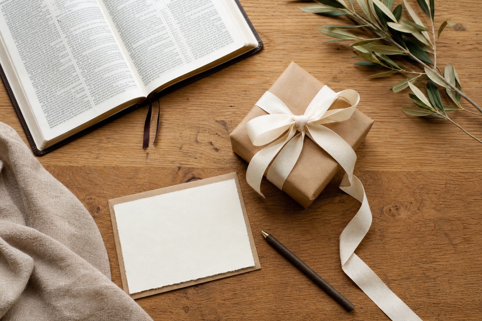 A wrapped gift, blank card, open Bible, and olive branches on a wooden table
