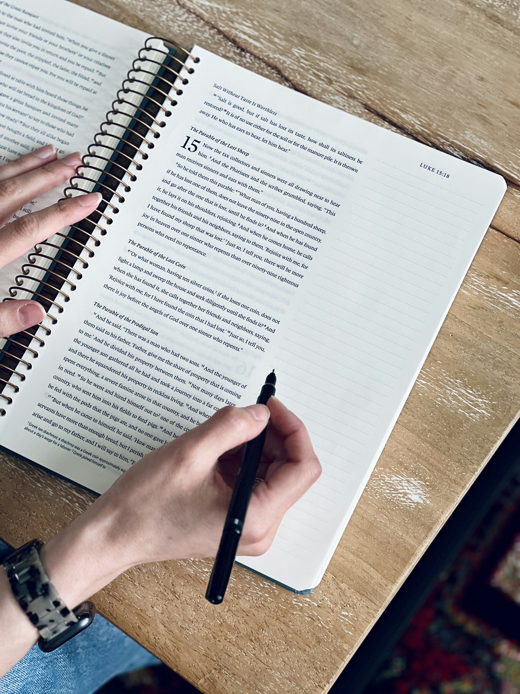 A person writing in a lined journal beside an open Bible