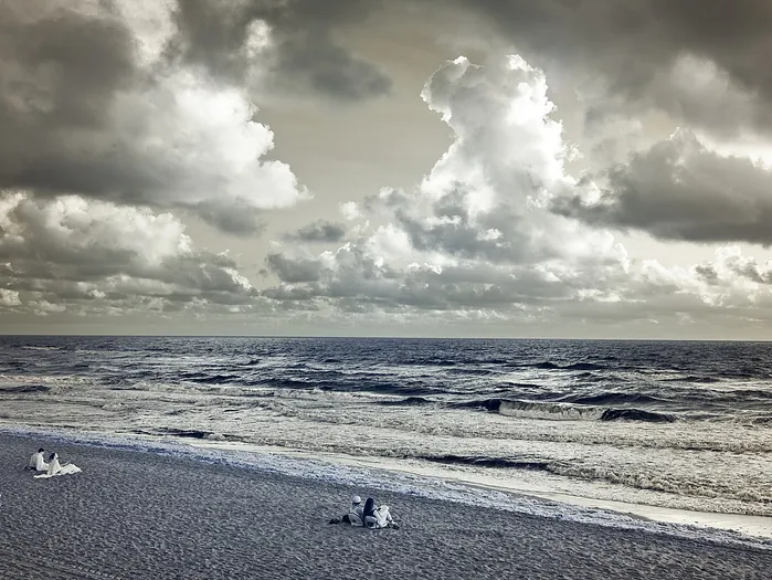 A blue-toned beach photograph with figures near the water.