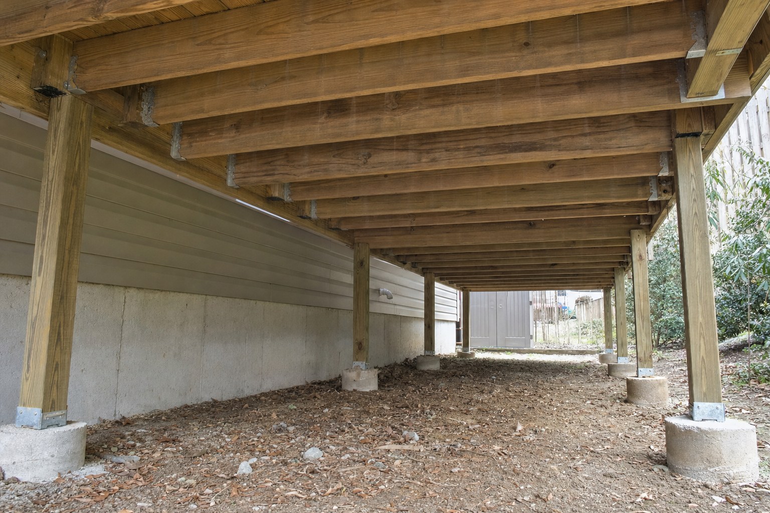 View beneath a residential wood deck showing joists, posts and metal connectors