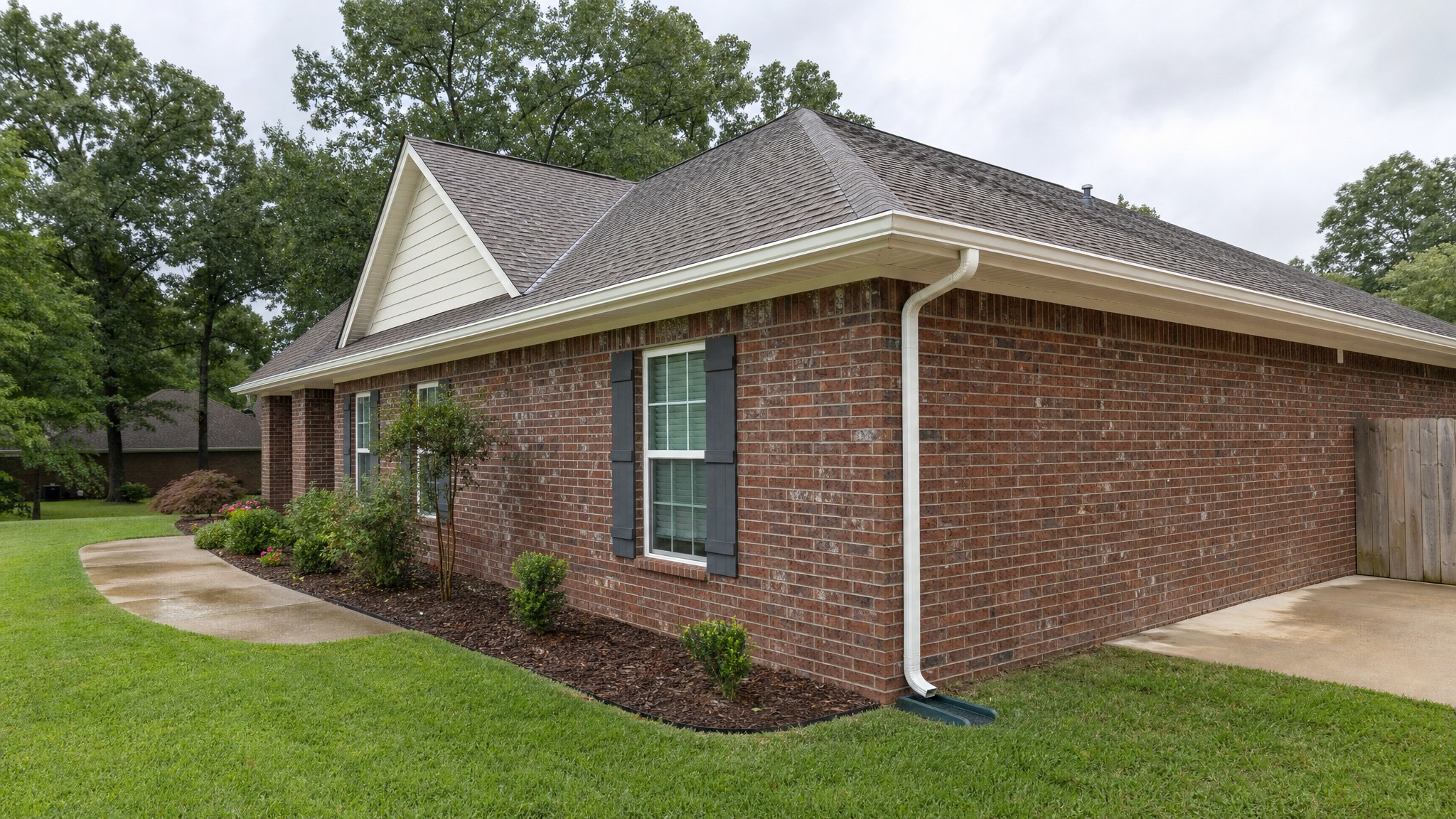Brick home with clean white gutters and a downspout directing water away from the foundation