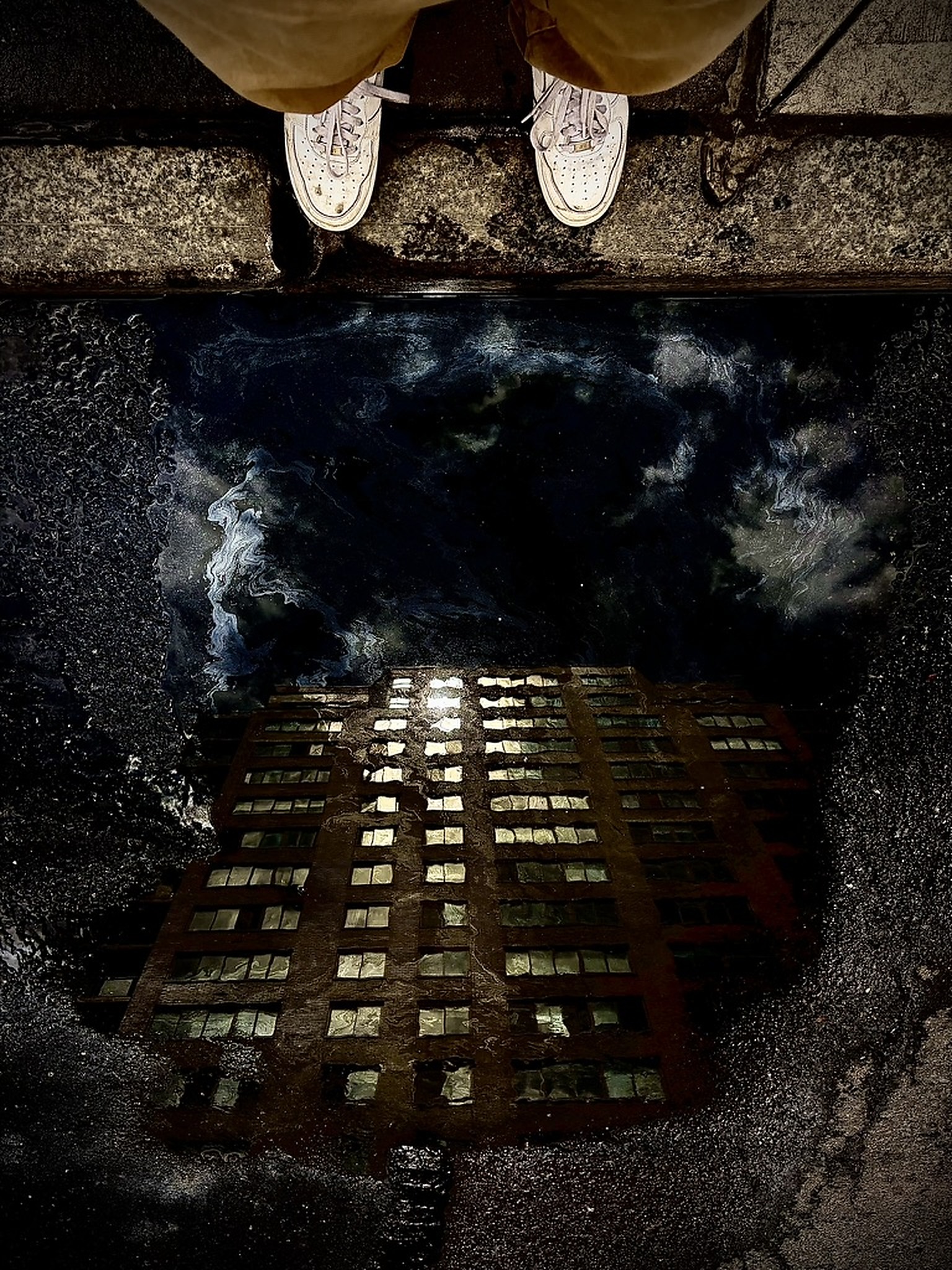 A building reflected in a rain puddle beneath passing shoes.