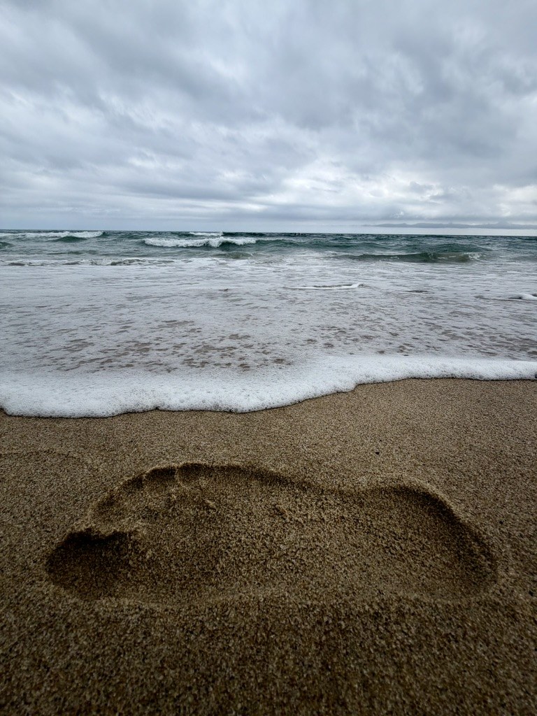 Waves washing over a footprint in sand
