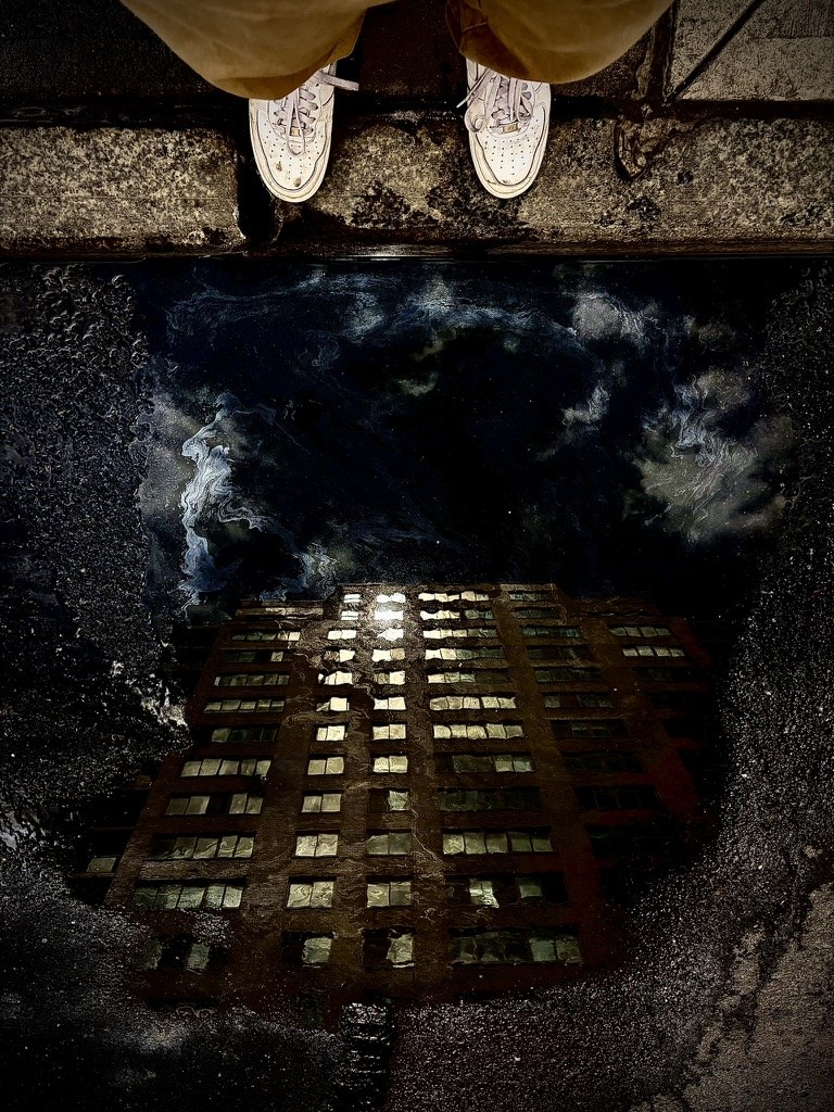 Building reflected in a puddle beneath shoes