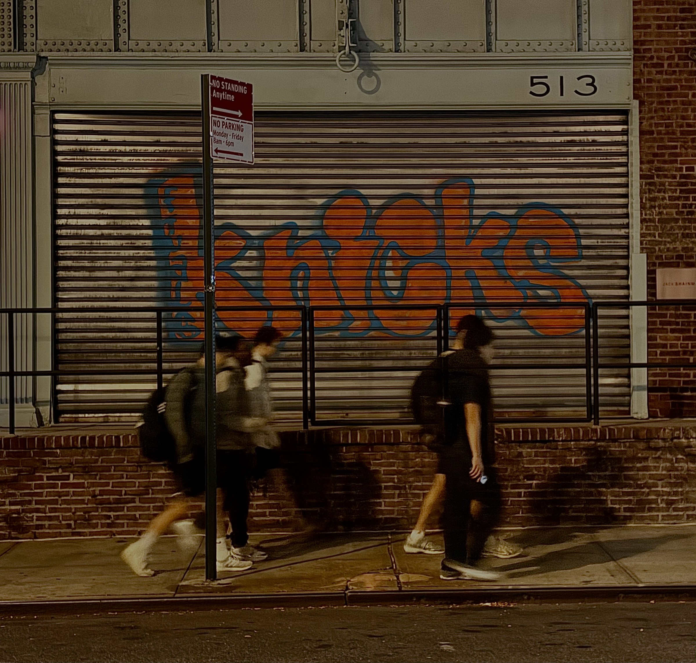 People walking past a graffiti-covered storefront at night