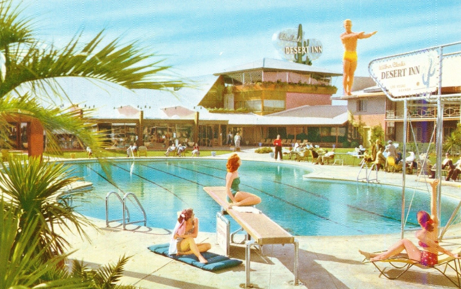A vintage scene of a pool area at the Desert Inn, featuring a diving platform with two women in swimsuits, one seated and one in a poised position, surrounded by palm trees and guests enjoying the sun.