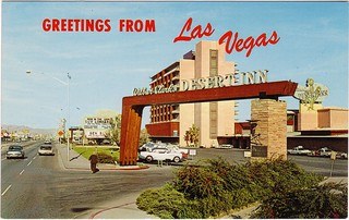 A vintage postcard of Las Vegas featuring the entrance of Desert Inn with the sign prominently displaying 'Greetings from Las Vegas'.