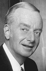 Black and white portrait of a man with light hair and a suit, smiling gently.
