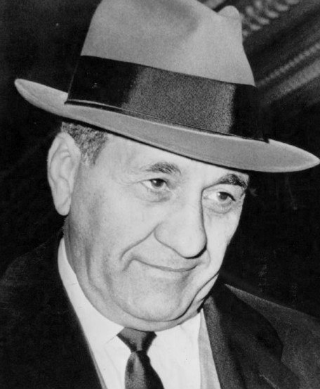 Black and white portrait of a man wearing a fedora hat and suit, appearing thoughtful.