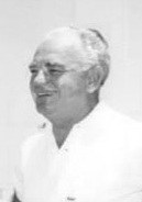A smiling older man in a white shirt, posed against a plain background.