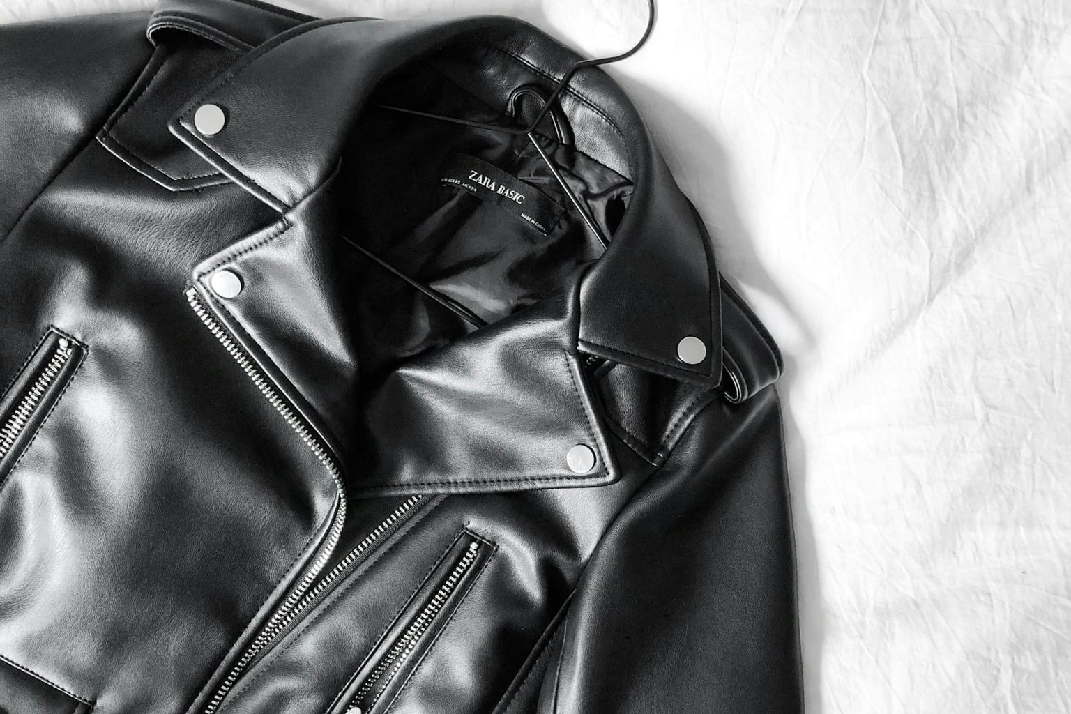 Black leather motorcycle jacket with silver hardware on a white backdrop