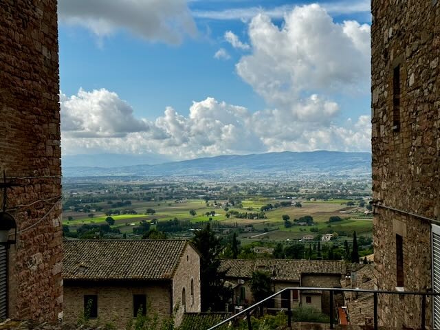 A broad valley and distant mountains framed by stone buildings