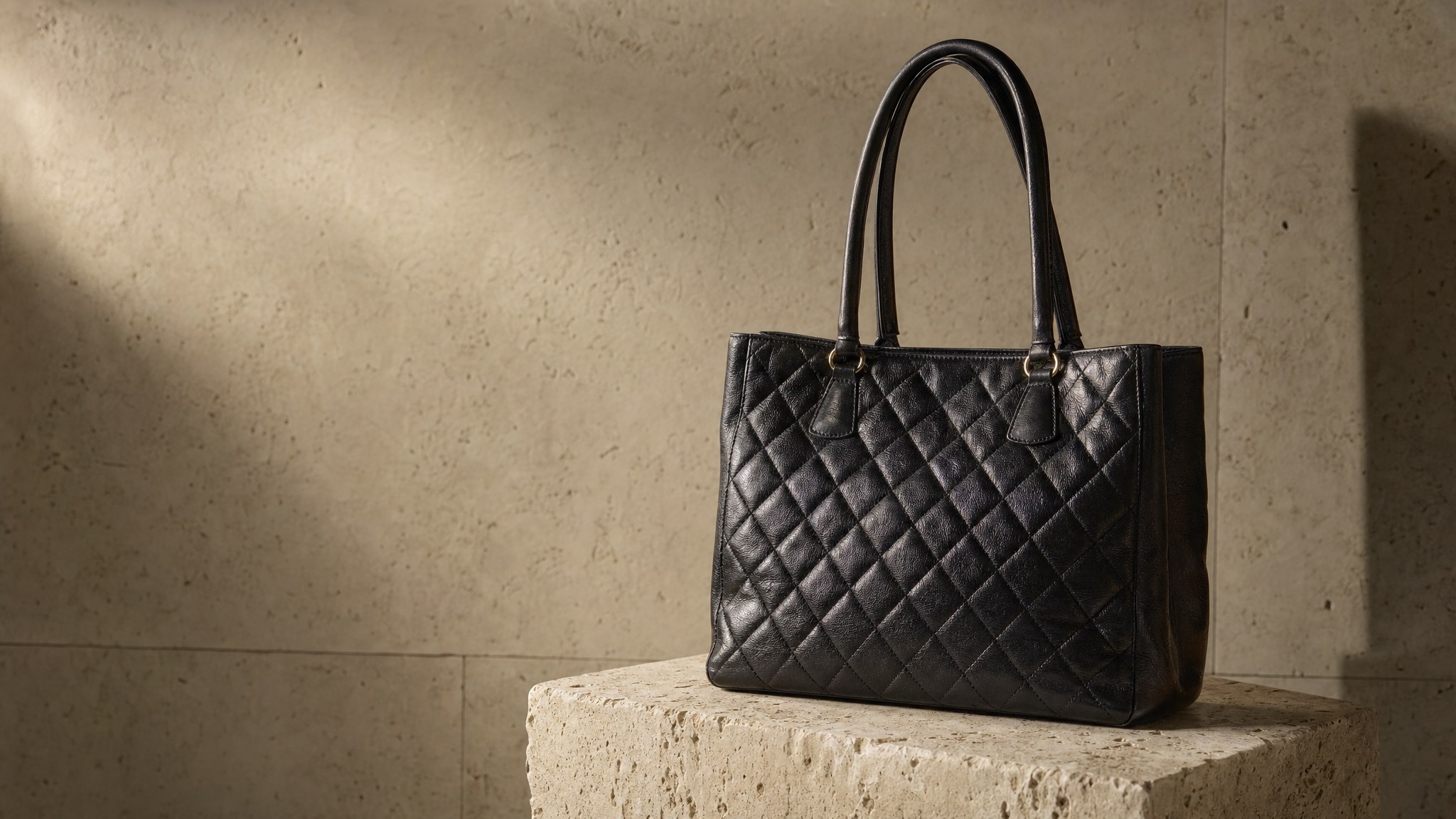 An unbranded black quilted leather tote on a limestone plinth