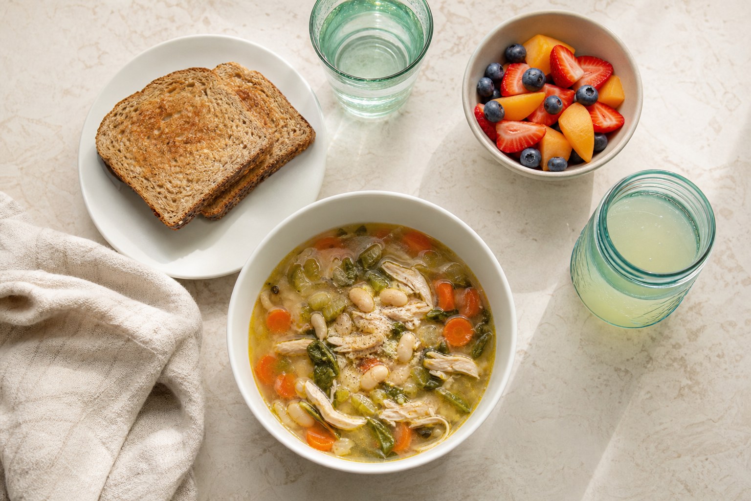 Soup, toast, fruit, water, and an electrolyte drink arranged as a simple recovery meal