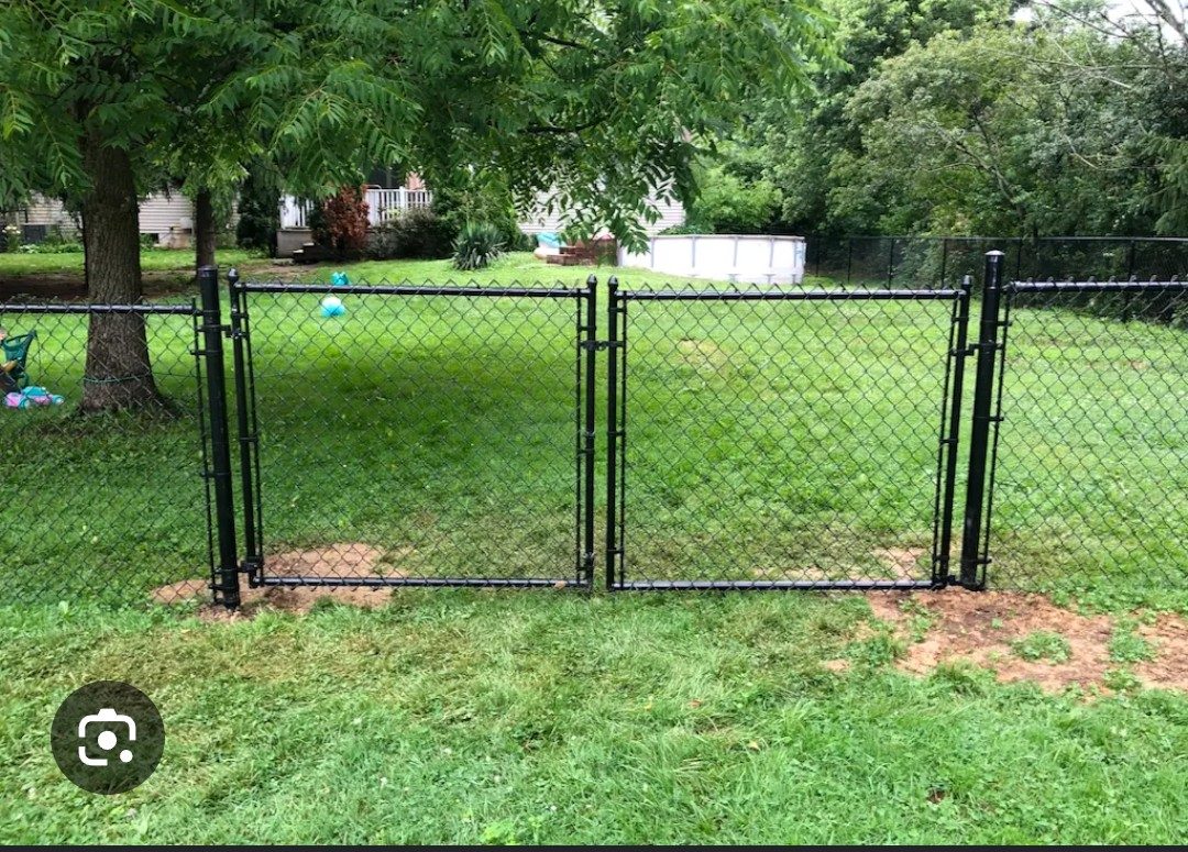 Black chain-link double gate opening into a green backyard