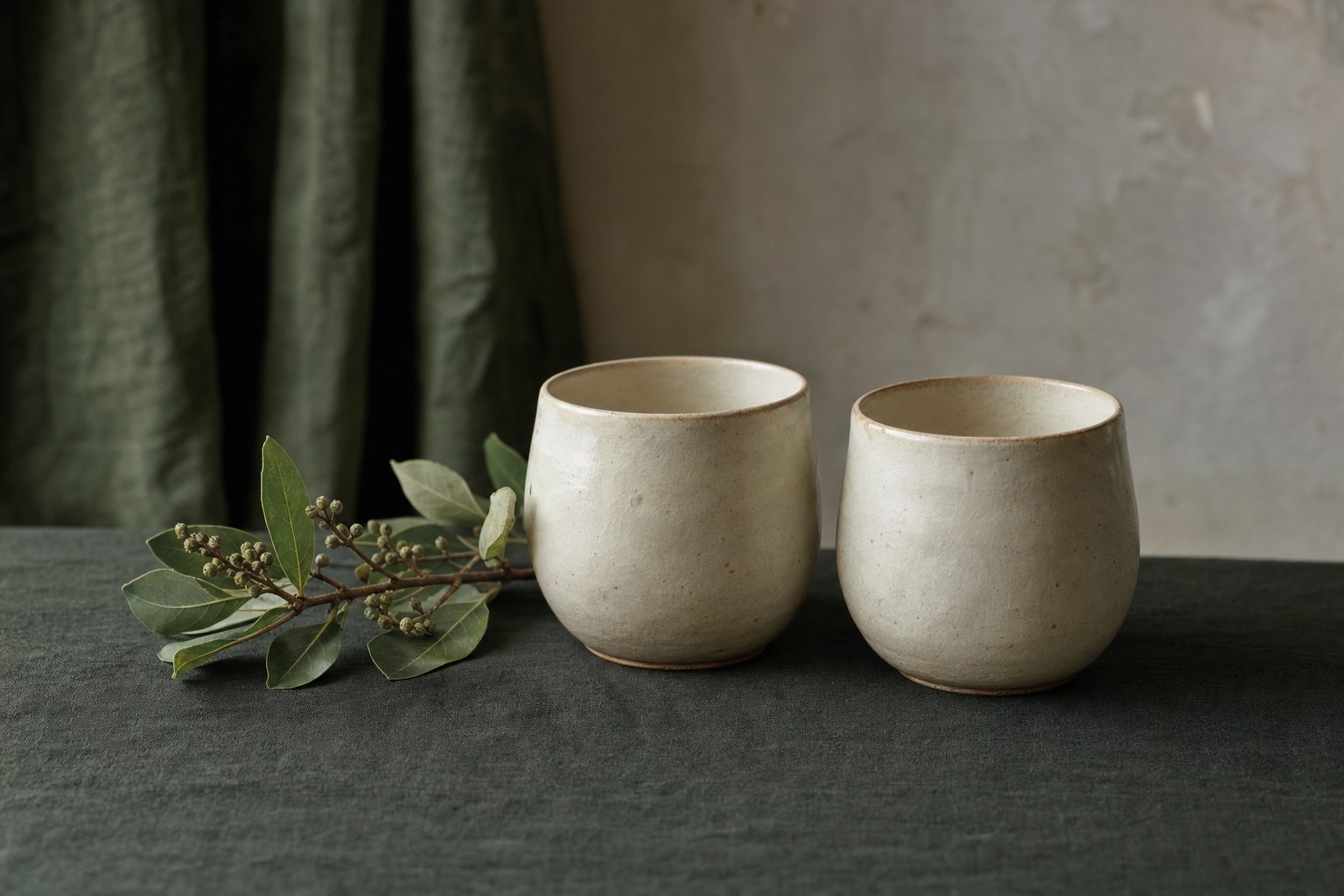 Two handmade ceramic cups together on green linen