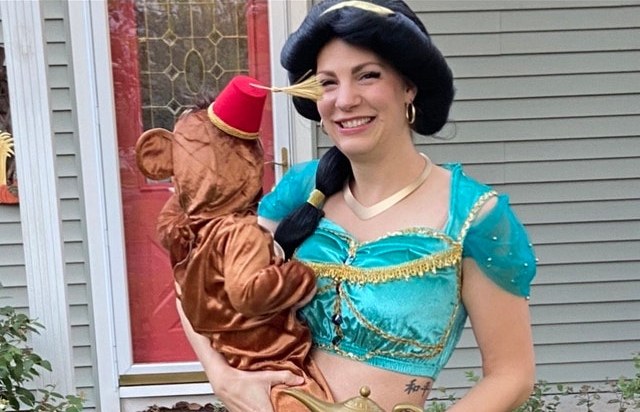 Woman dressed as Princess Jasmine holding a child in an Aladdin costume with a red mini hat