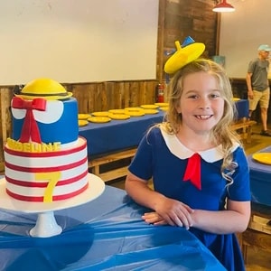 Girl wearing a yellow beret beside a themed birthday cake