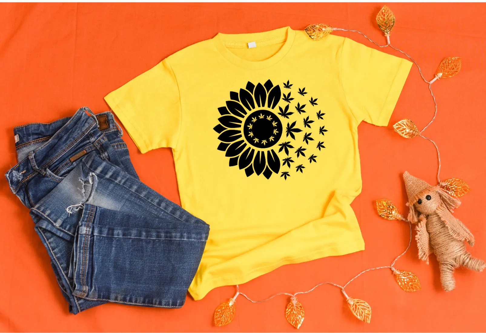 Bright yellow shirt with sunflower design and jeans on orange background.