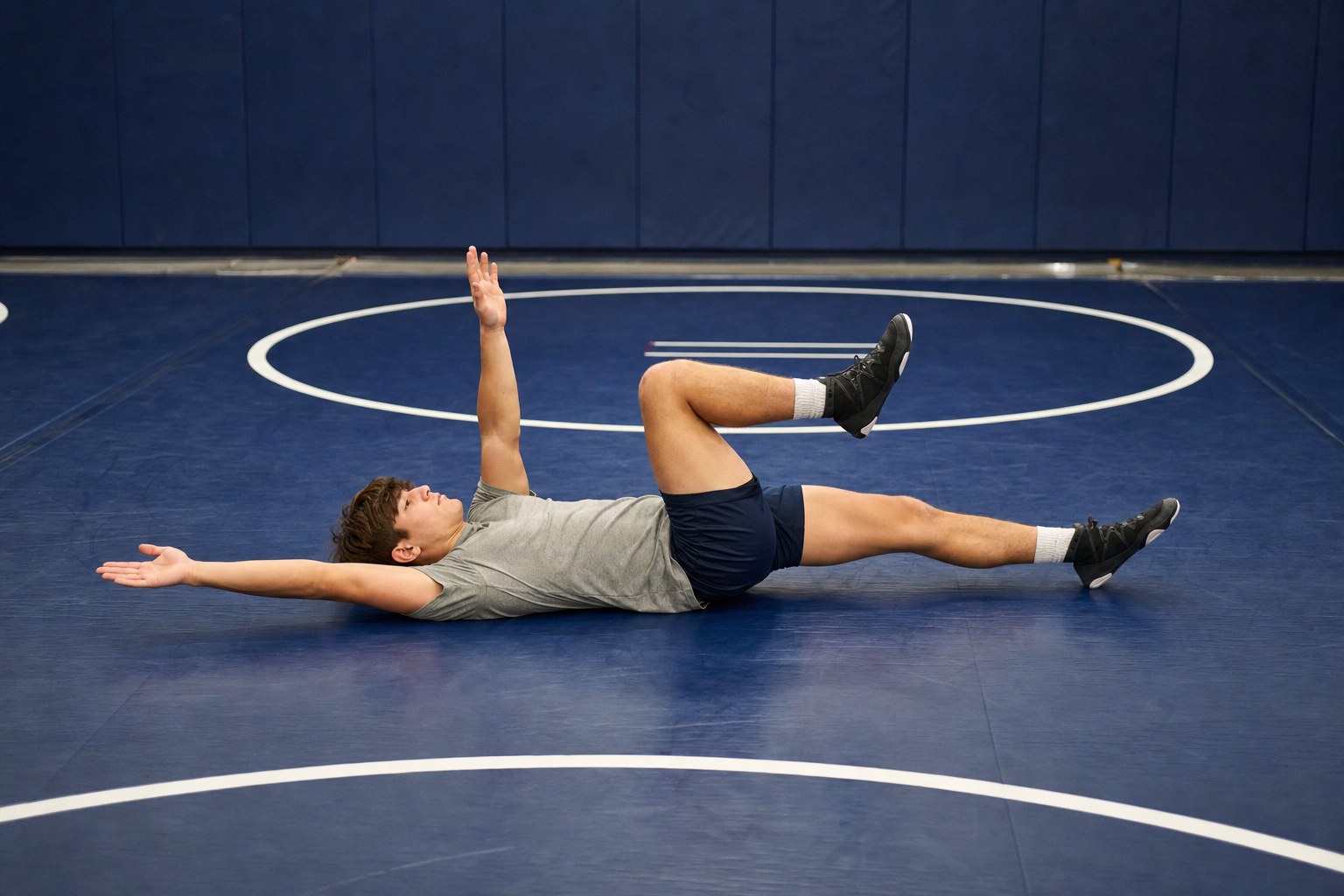 A wrestler performing a controlled dead bug exercise on a practice mat