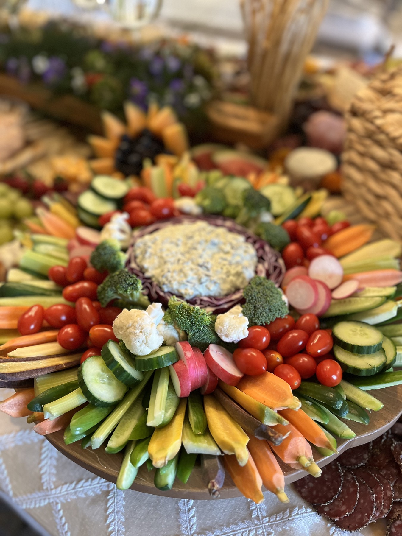 Fresh vegetable board with cucumbers, carrots, radishes, tomatoes, broccoli, cauliflower and a central dip