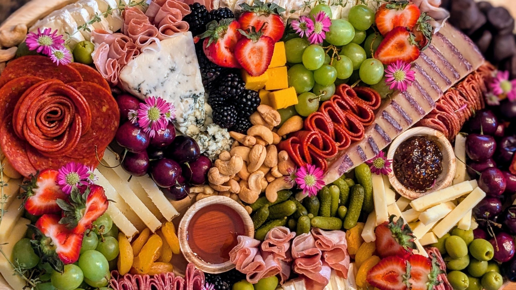 A Yellow House Grazing board filled with fruit, cheeses, charcuterie and edible flowers