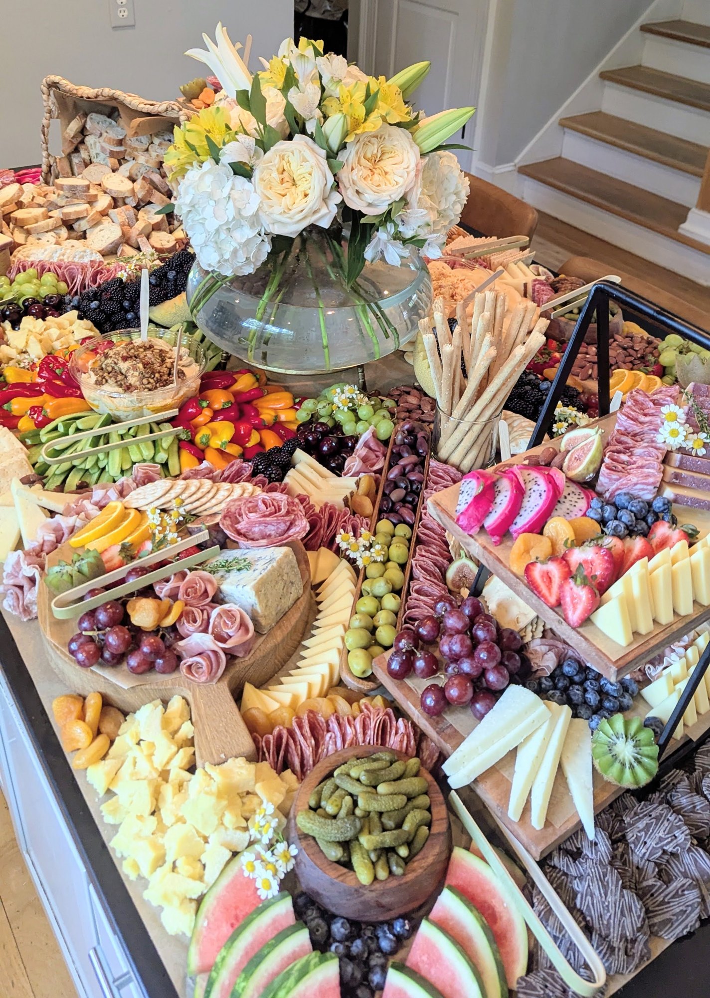 Grazing table with colorful fruit, cheeses and a white and yellow floral centerpiece