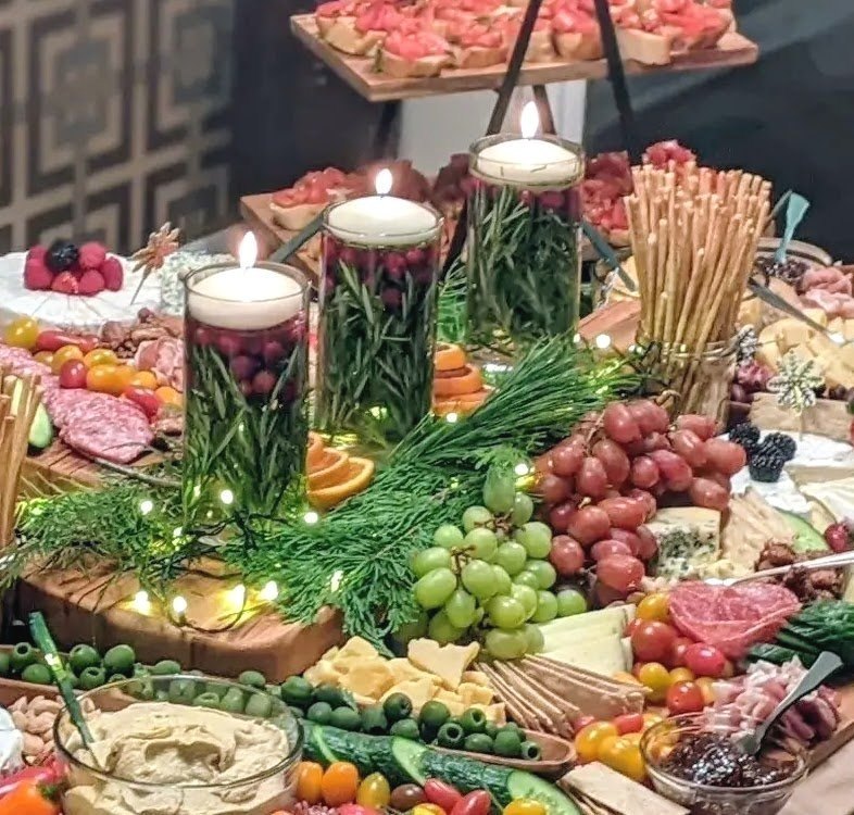 Grazing table with glowing candles, greenery, fruit, cheeses and charcuterie