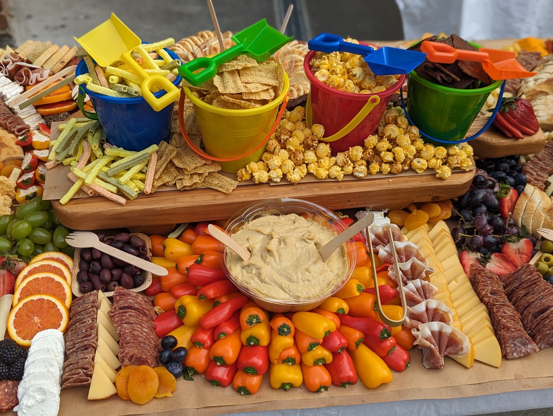 Playful grazing table with colorful beach pails, crackers, popcorn, vegetables and charcuterie