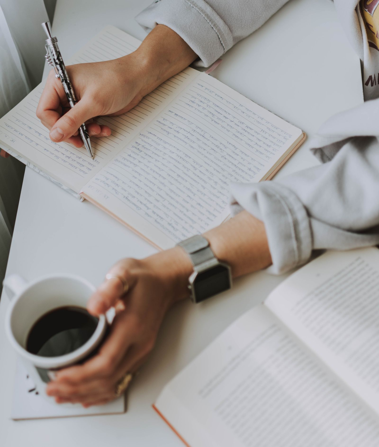 A person writing in a notebook beside a cup of coffee