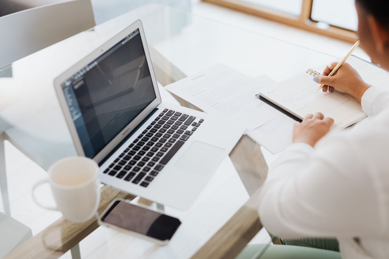 A person planning in a notebook beside a laptop and coffee