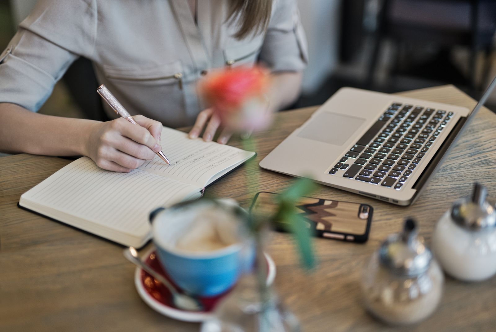 A person writing in a notebook beside a laptop and coffee