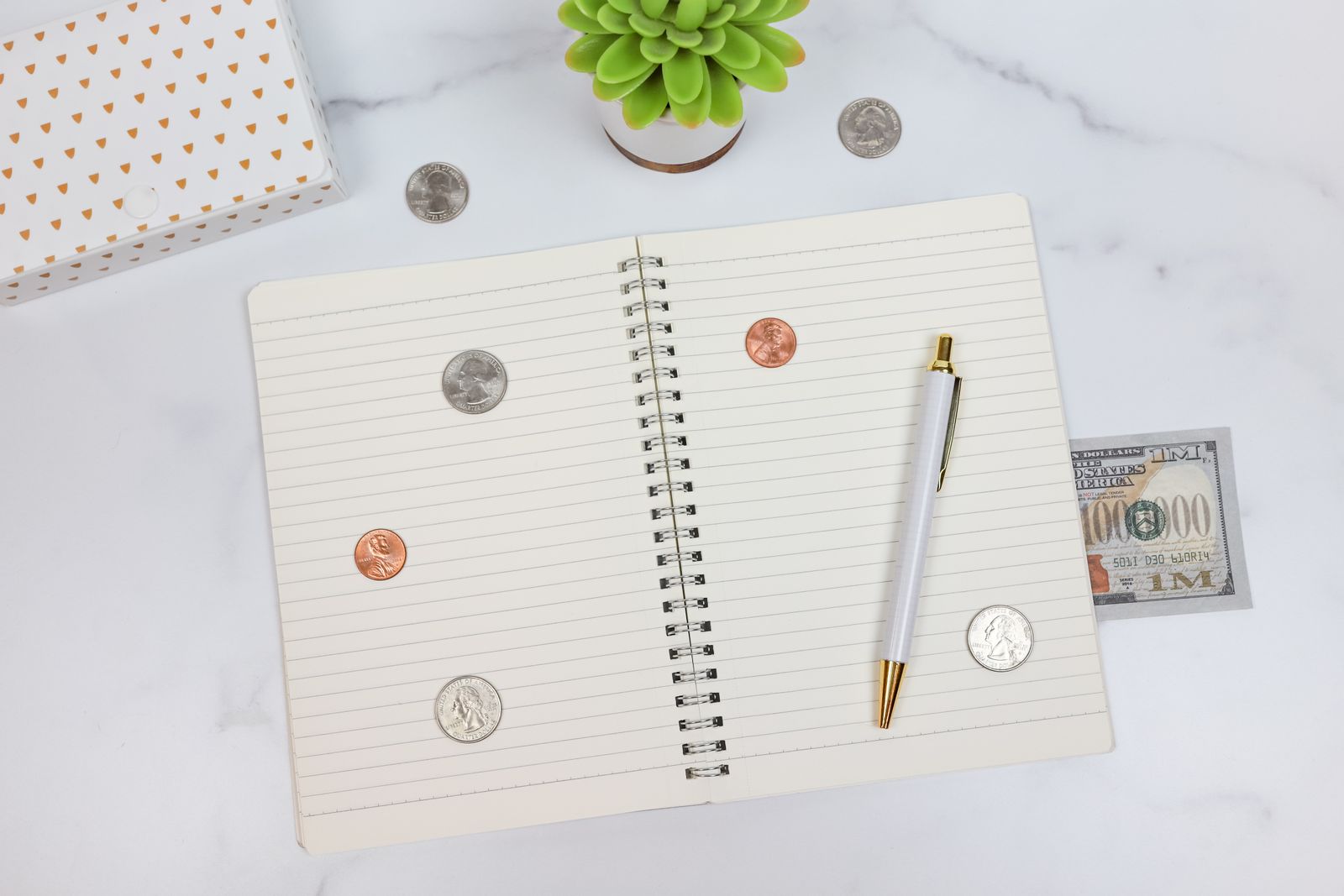 An open notebook and pen arranged with a few coins and a small plant
