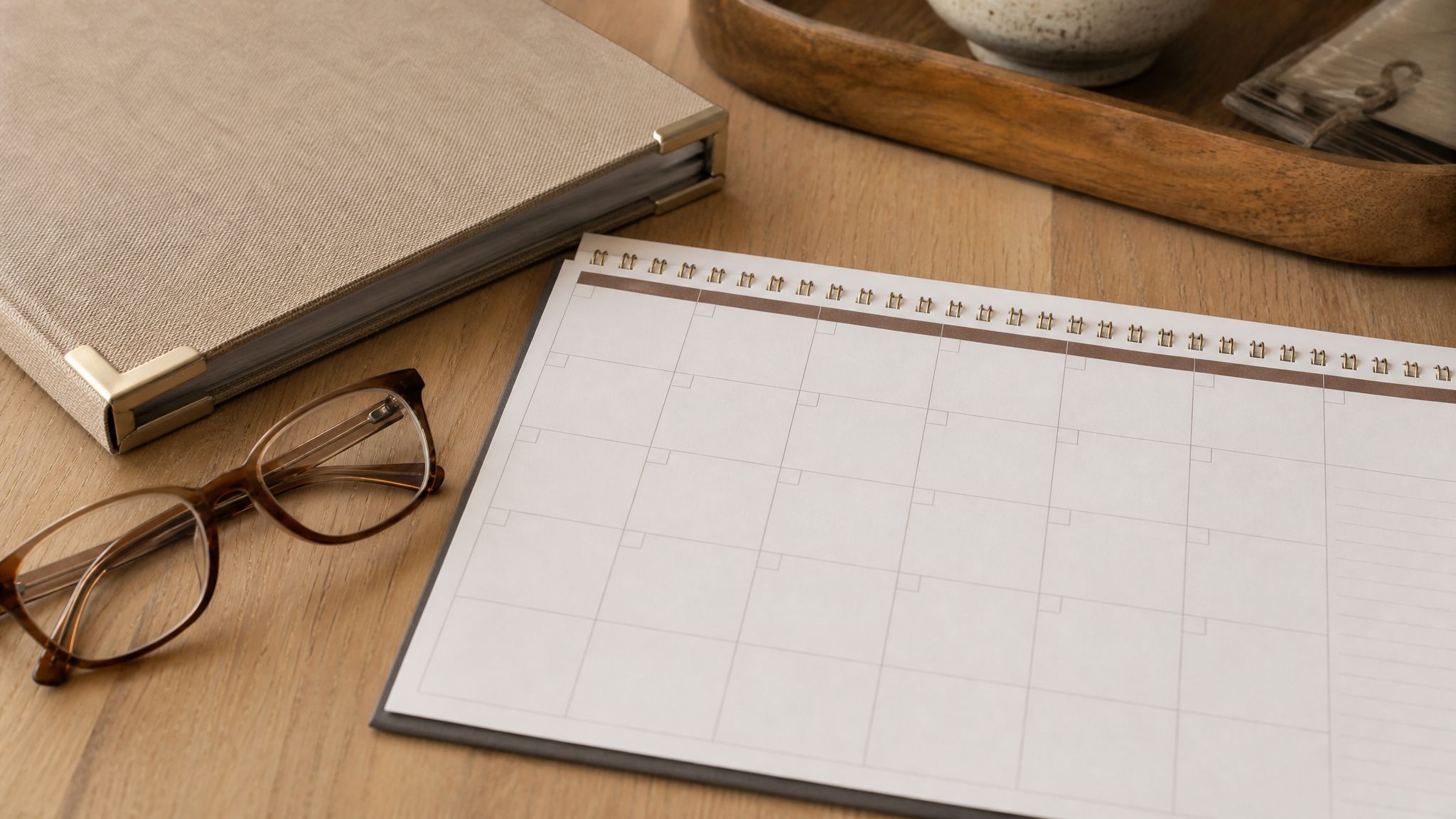 Blank planning calendar, binder, and reading glasses on a kitchen table.