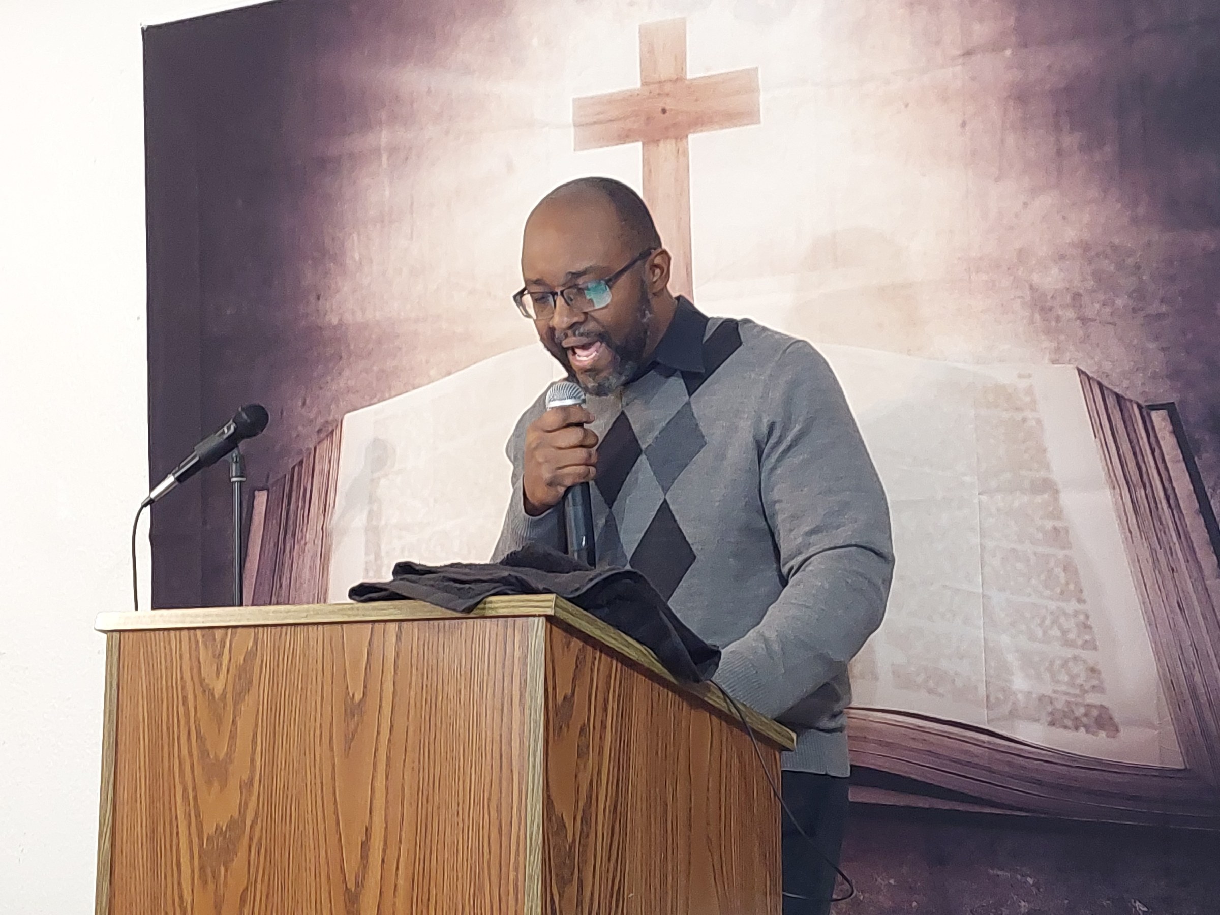 Pastor teaching from an open Bible beneath a cross