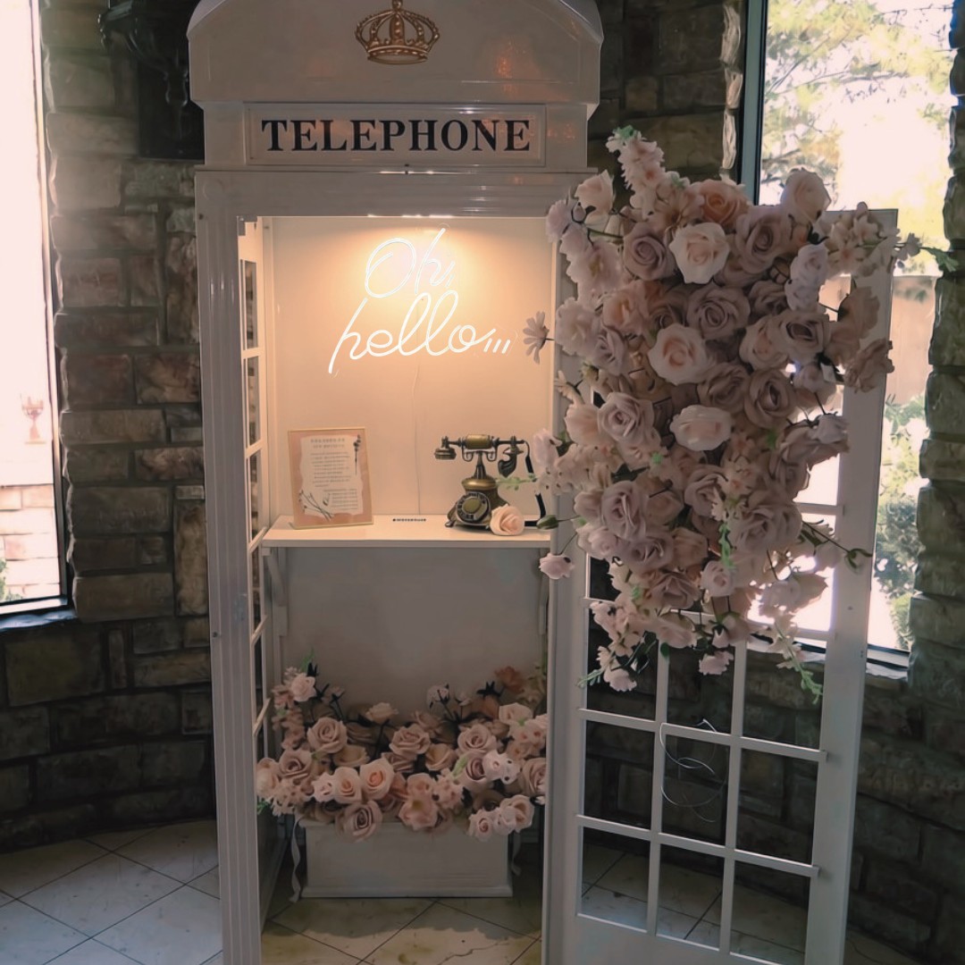 White telephone booth enclosure with pink flowers and a brass rotary guestbook phone