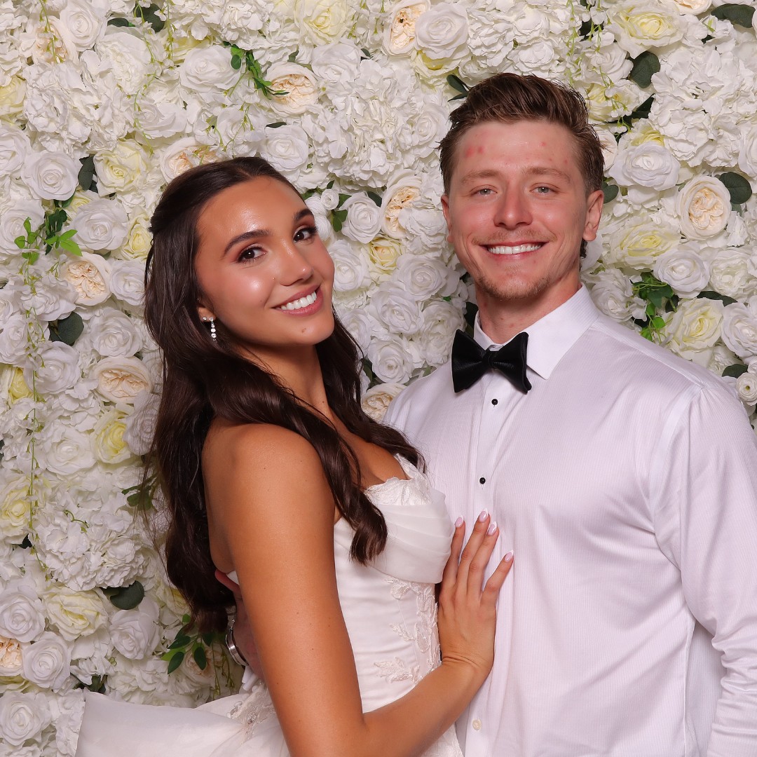 Bride and wedding guest photographed against a white flower wall at a Phoenix wedding