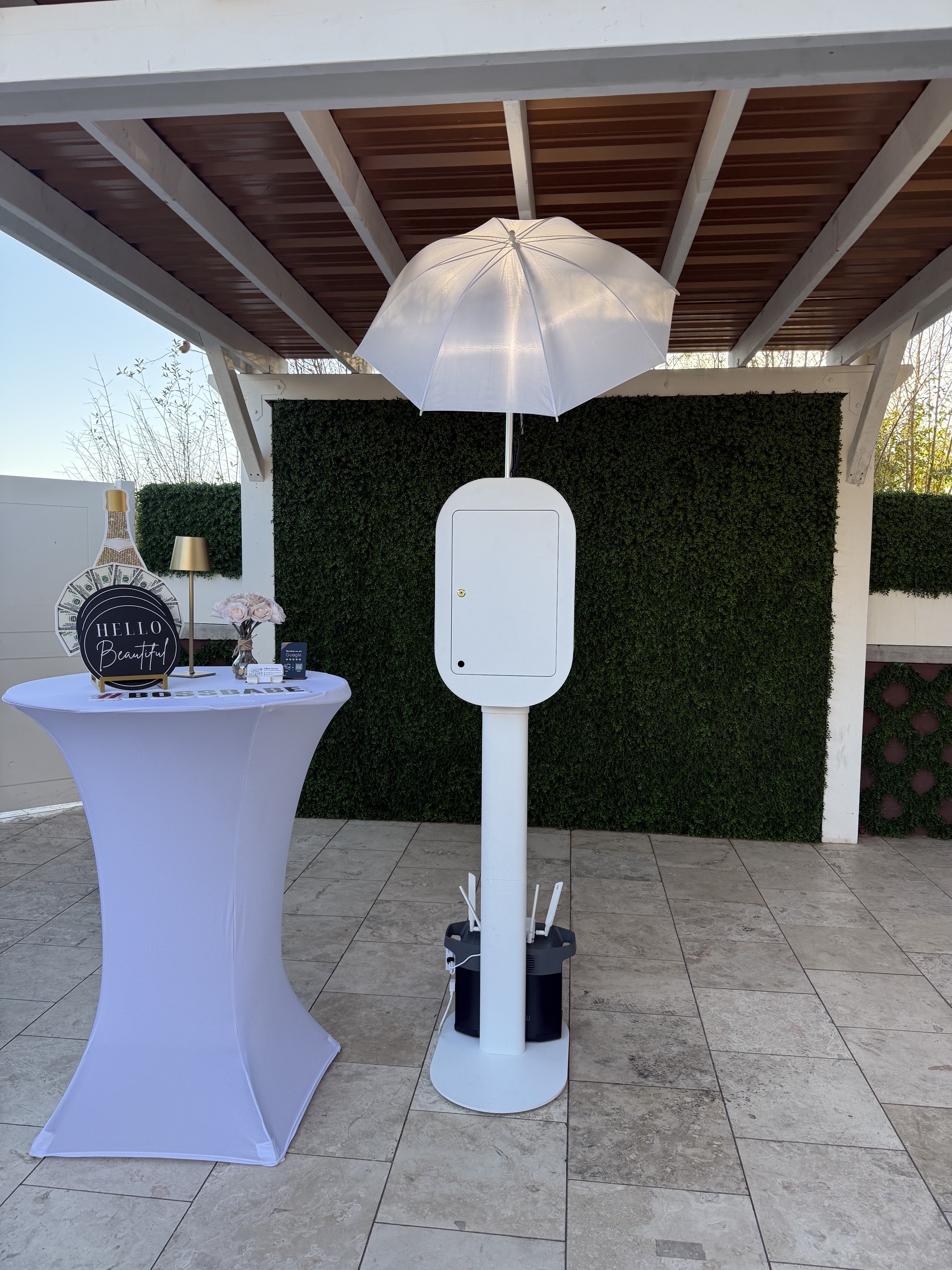 The Luxe white DSLR photo booth set up with umbrella lighting and a greenery wall at Dolce Events in Scottsdale, Arizona