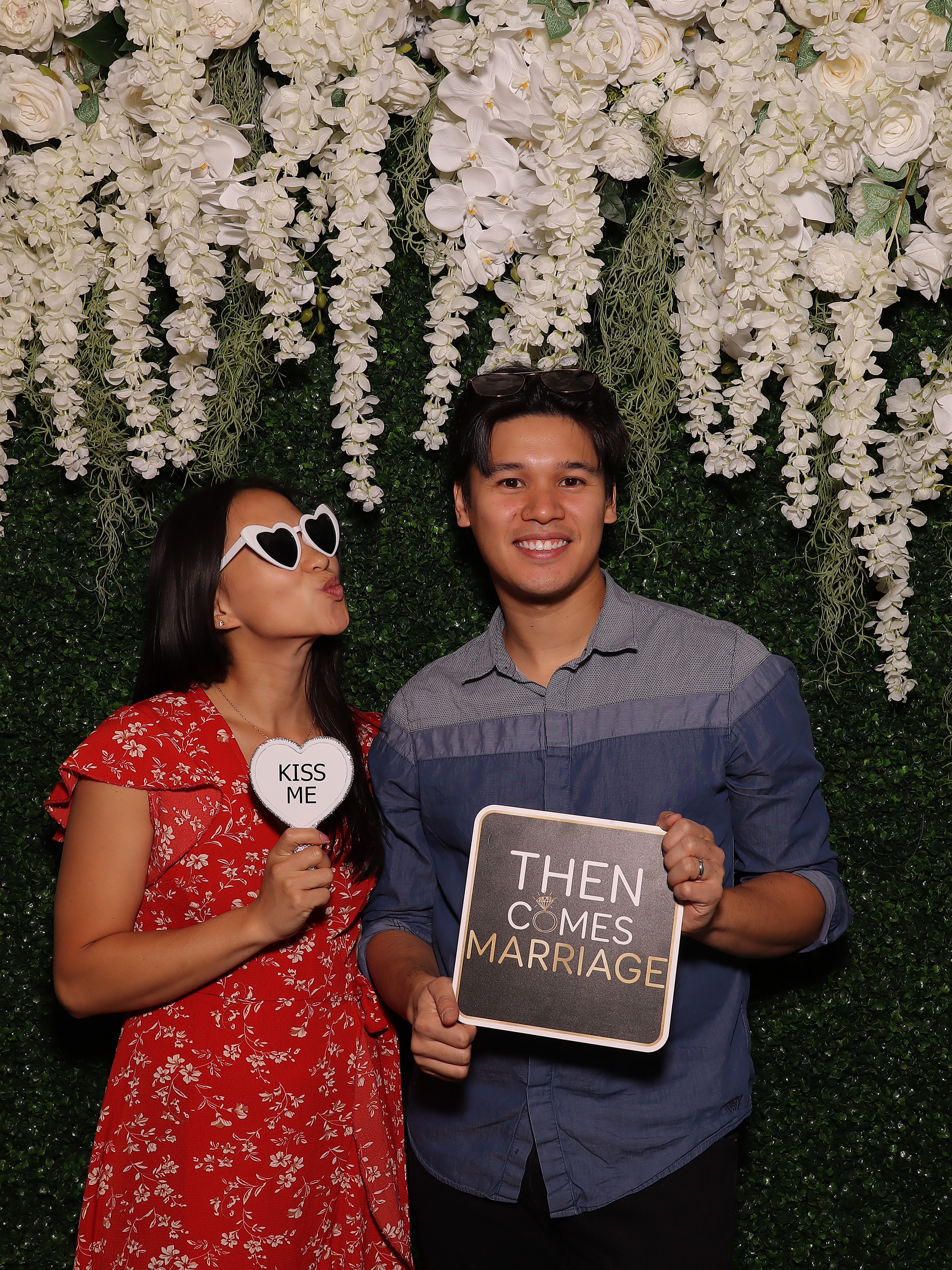Couple posing in front of a floral and greenery Photo Booth backdrop