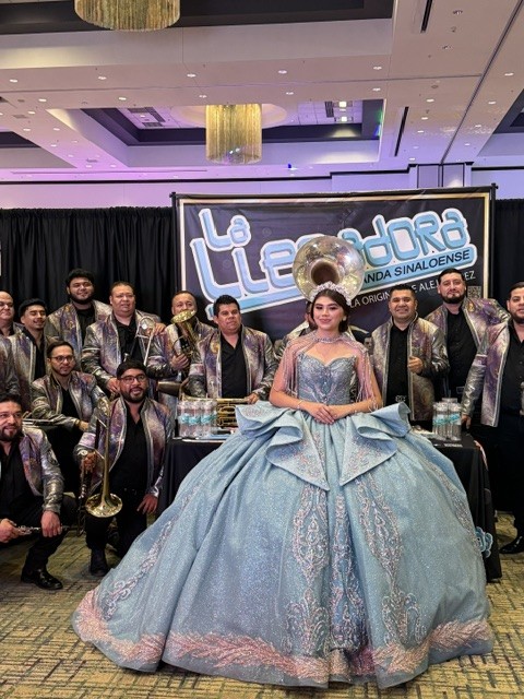 Quinceañera in a blue formal gown pictured with a live band at the 2026 Quinceañera and Wedding Expo in Glendale, Arizona