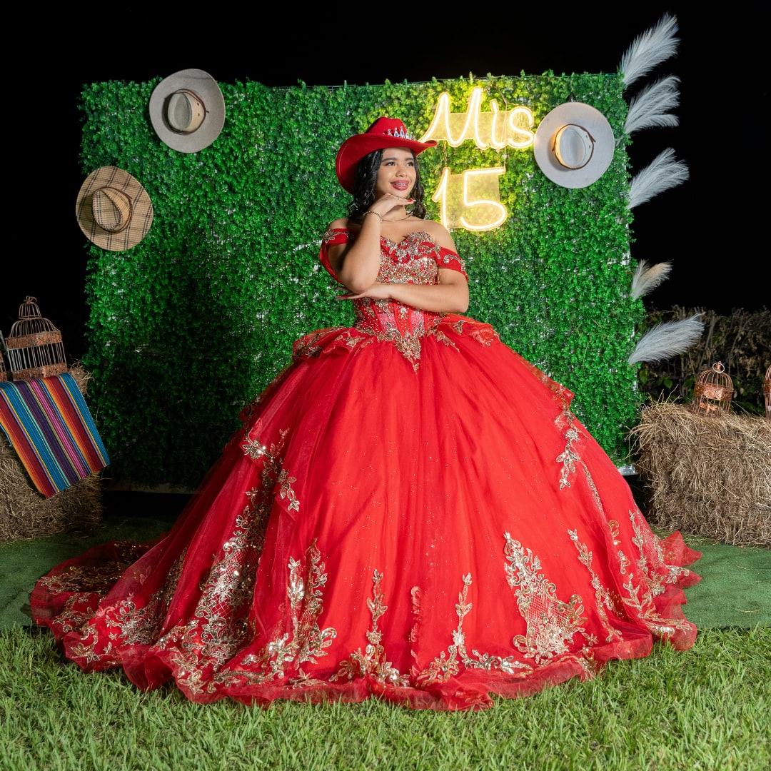 Quinceañera in a red gown posing in front of a greenery photo booth backdrop