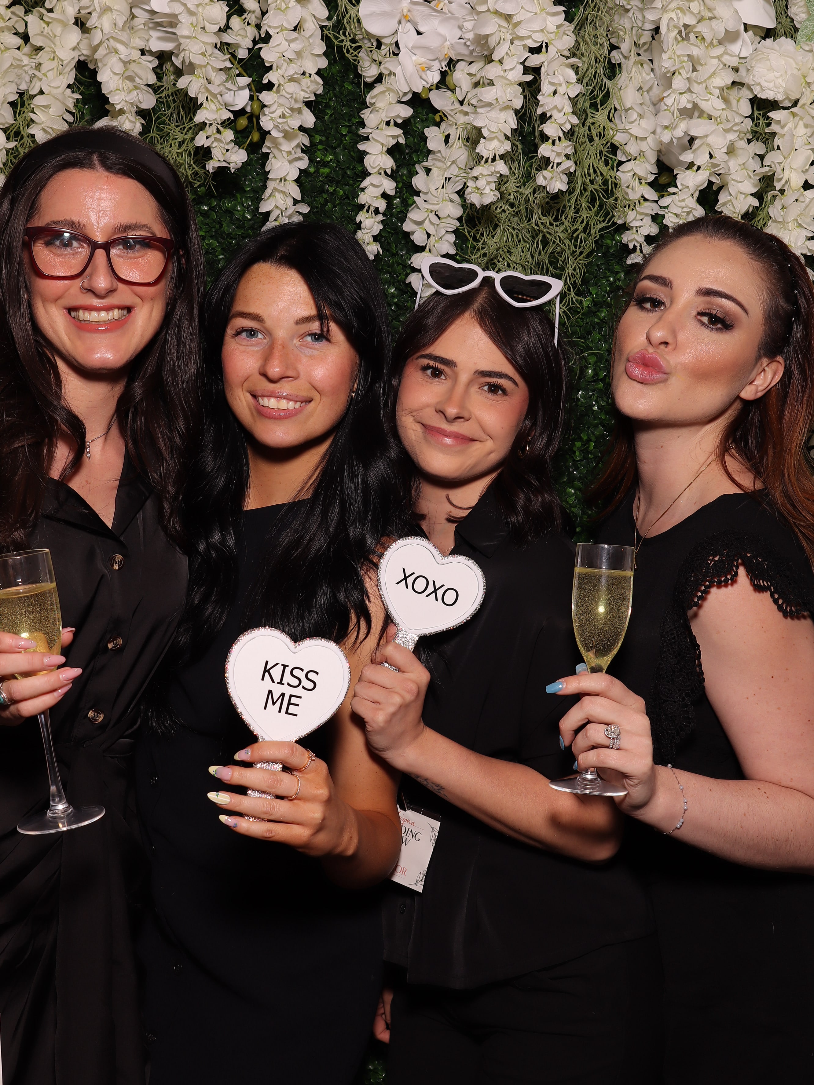 Three guests posing in front of a white floral and greenery Photo Booth backdrop