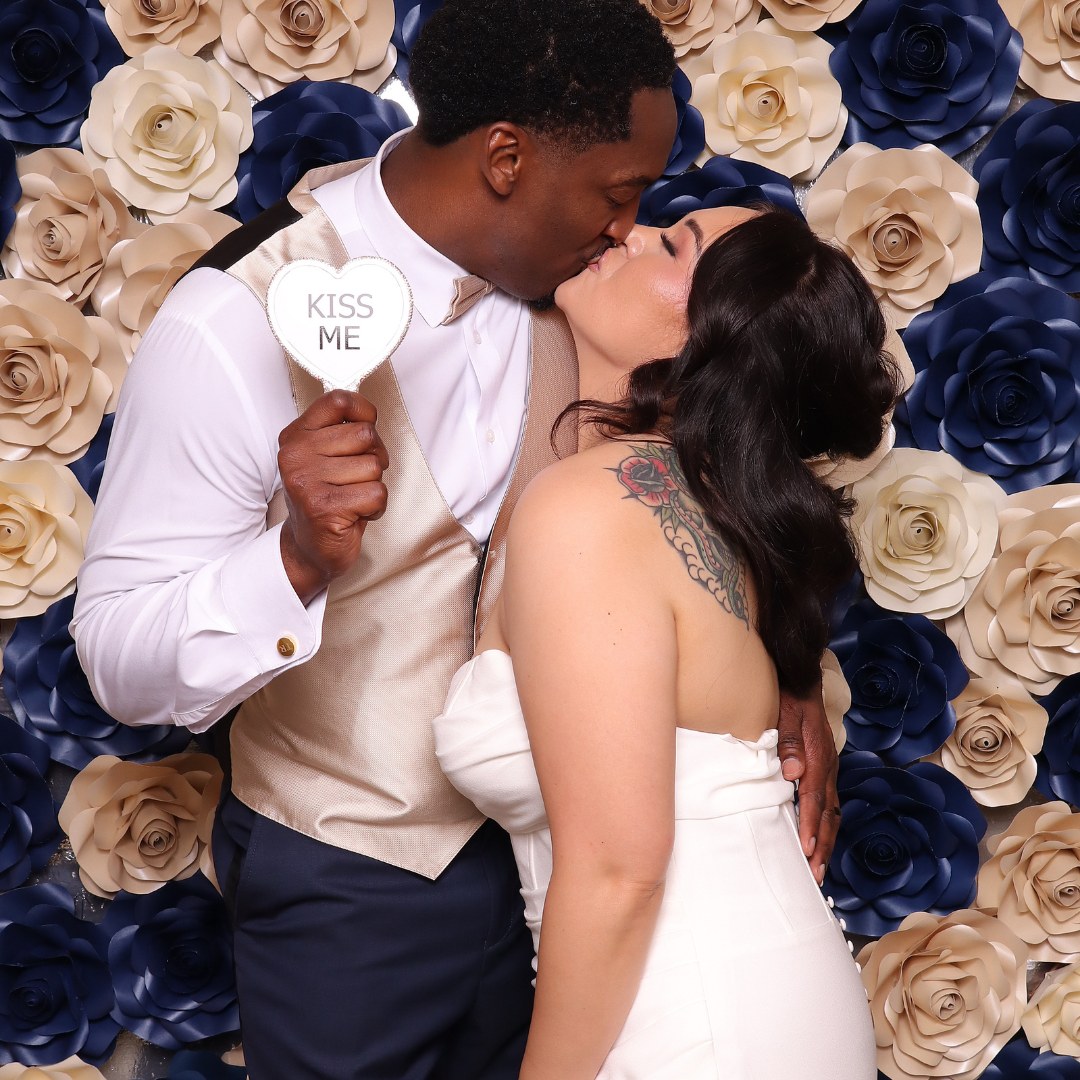 Newlyweds sharing a kiss in front of a floral wall