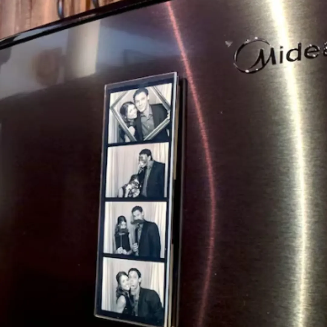 Acrylic magnet photo frame holding a photo booth film strip on a refrigerator
