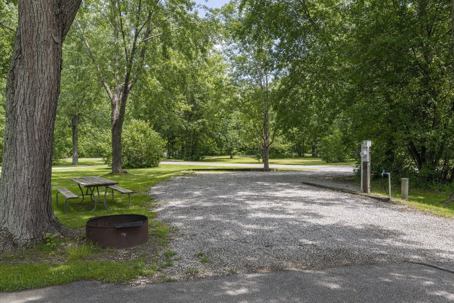 Campground RV site showing a gravel pad, hookups, picnic table, and fire ring