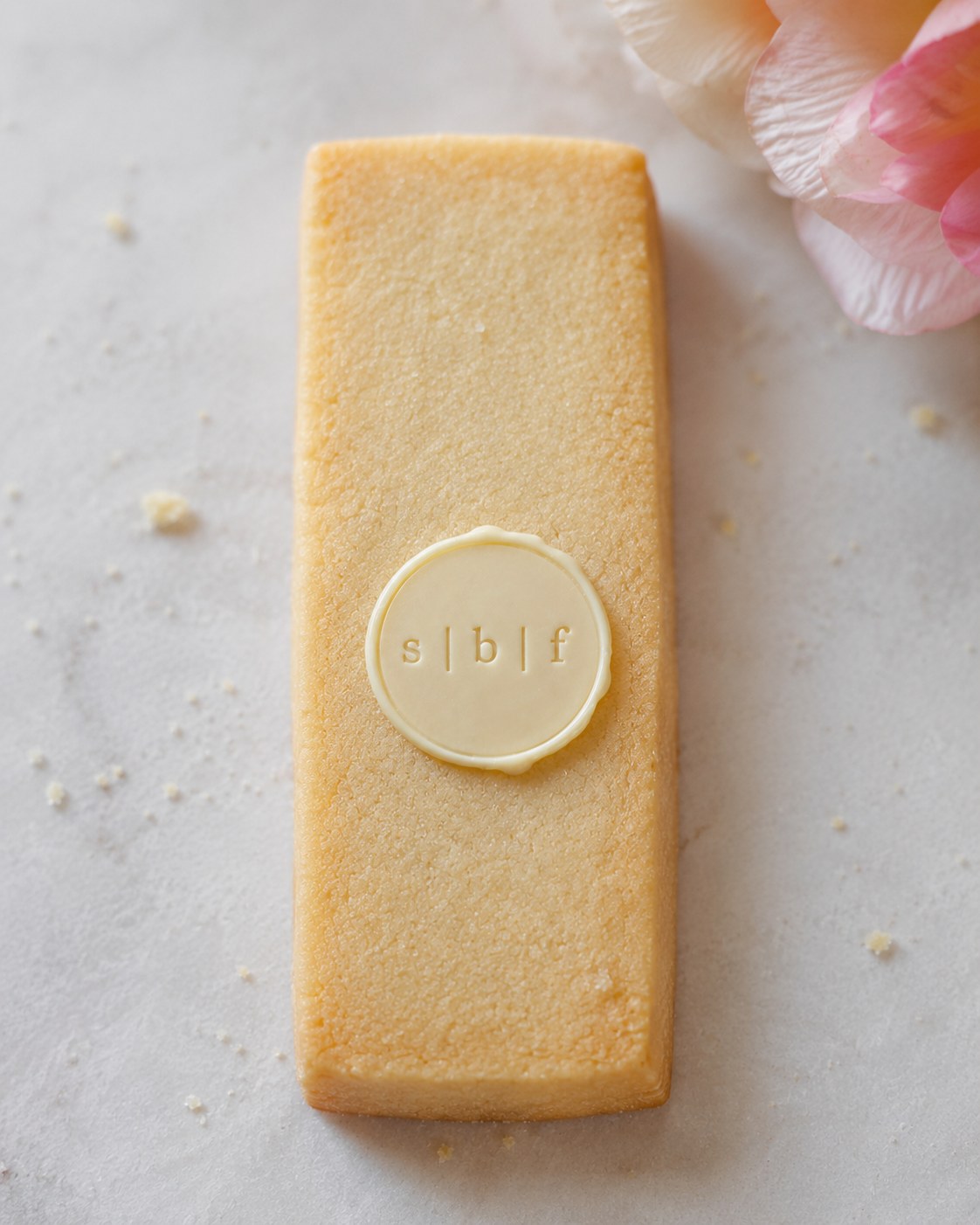 A buttery shortbread cookie with a white chocolate Sugar Butter Flower seal and pink flowers