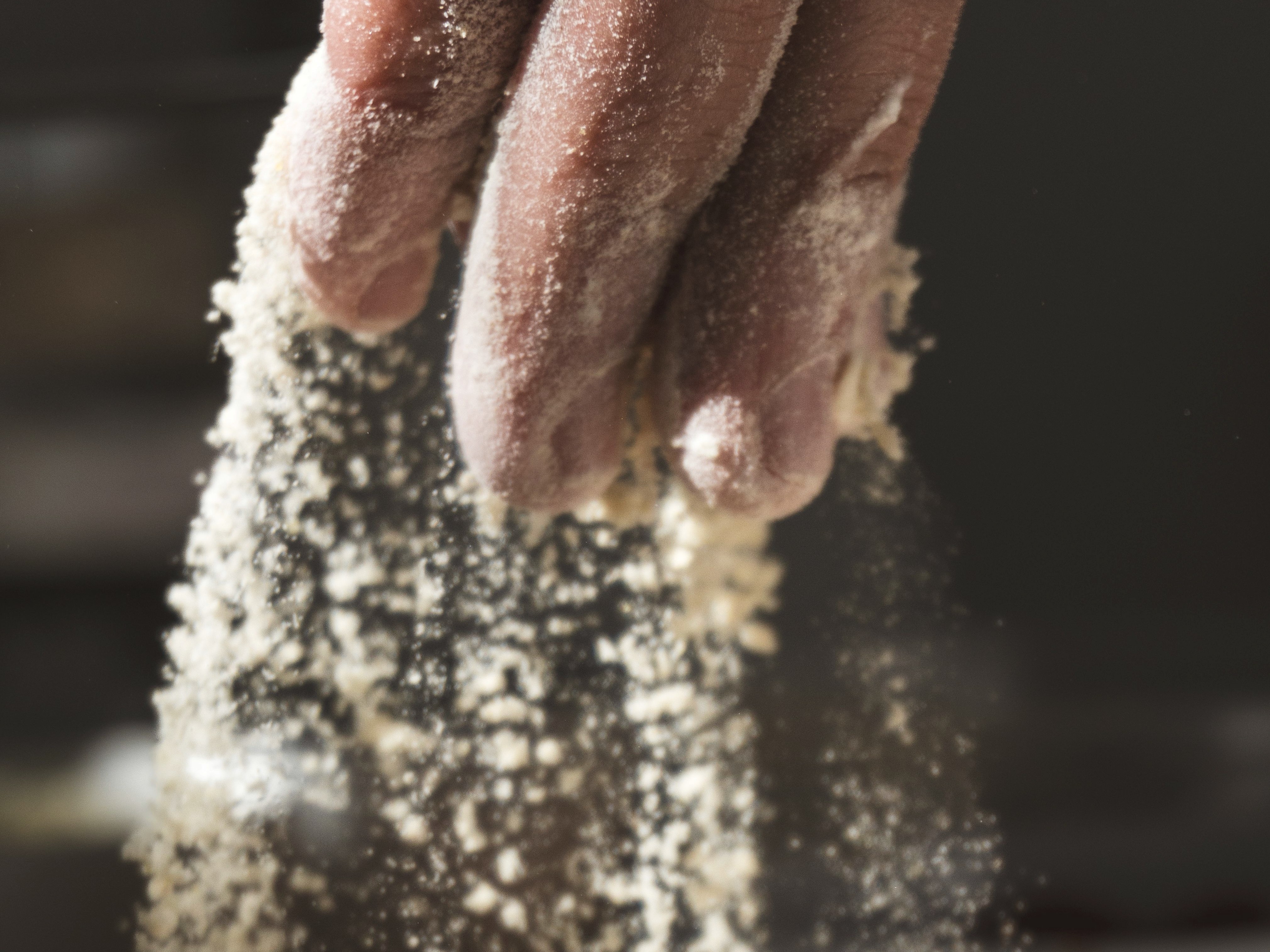 A baker's hand dusted with flour over a mixing bowl